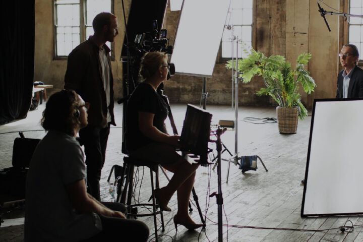 A futuristic office setting with a diverse group of professionals collaborating around a large touch-screen table displaying digital data and analytics. The background features sleek, modern office furniture and large windows with natural light. Prominently displayed is the Konica Minolta logo, emphasizing innovation and advanced technology in a corporate environment. The atmosphere conveys a sense of teamwork, productivity, and cutting-edge solutions.