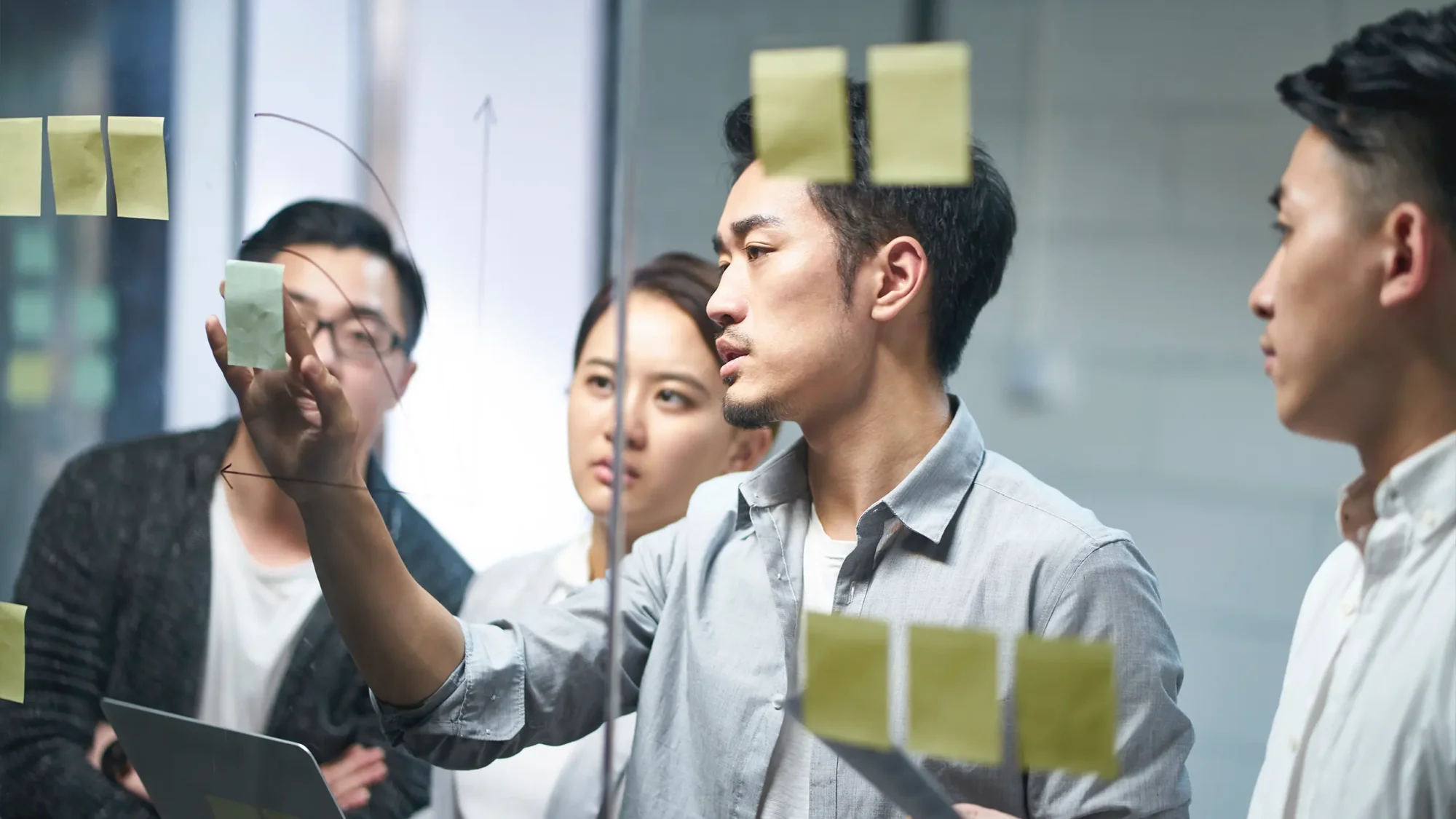 A group of Asian business professionals collaborating on a project, engaged in discussion and teamwork at a modern office.