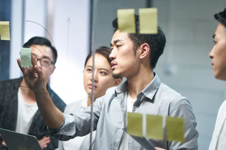 A group of Asian business professionals collaborating on a project, engaged in discussion and teamwork at a modern office.