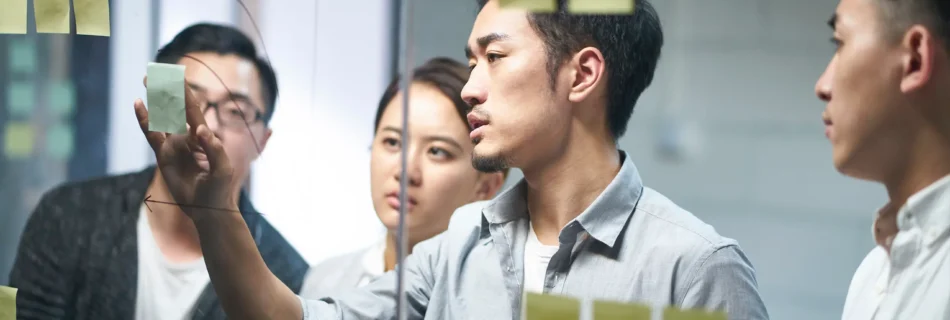 A group of Asian business professionals collaborating on a project, engaged in discussion and teamwork at a modern office.