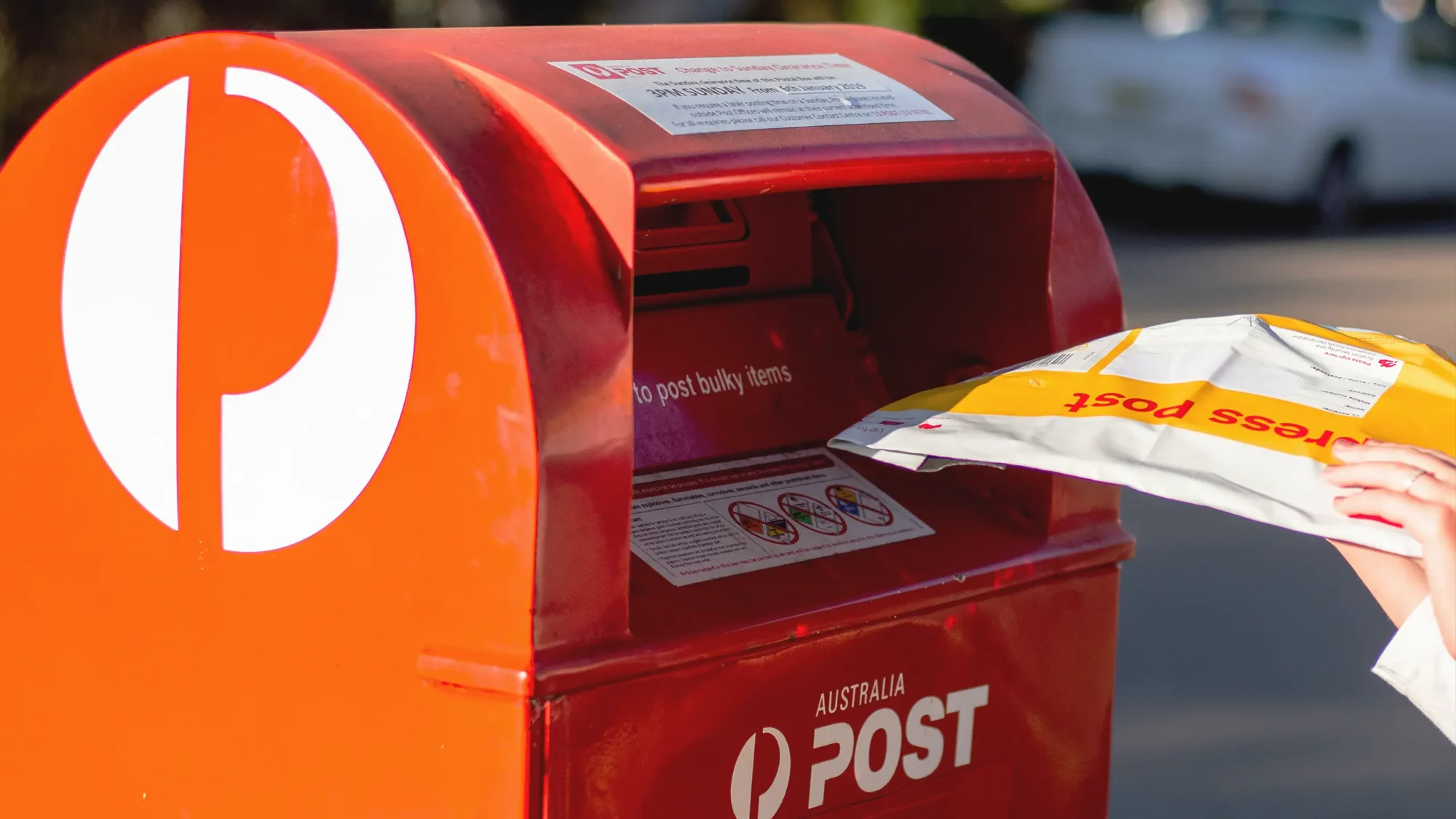 person putting their mail into a red Australia Post, post box