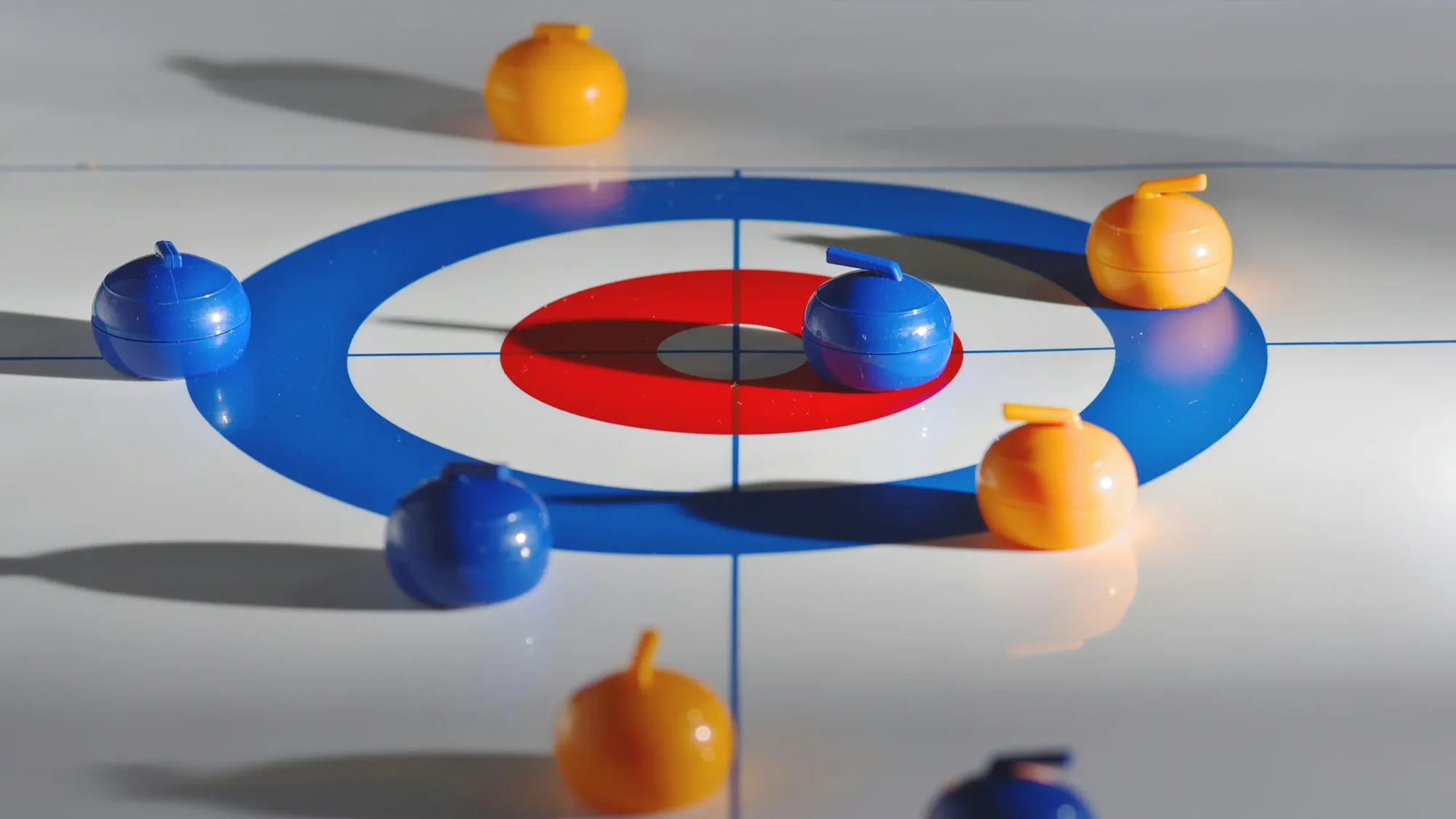 Mini curling game board with six stones, three orange and three blue, on a white surface with a red and blue target.